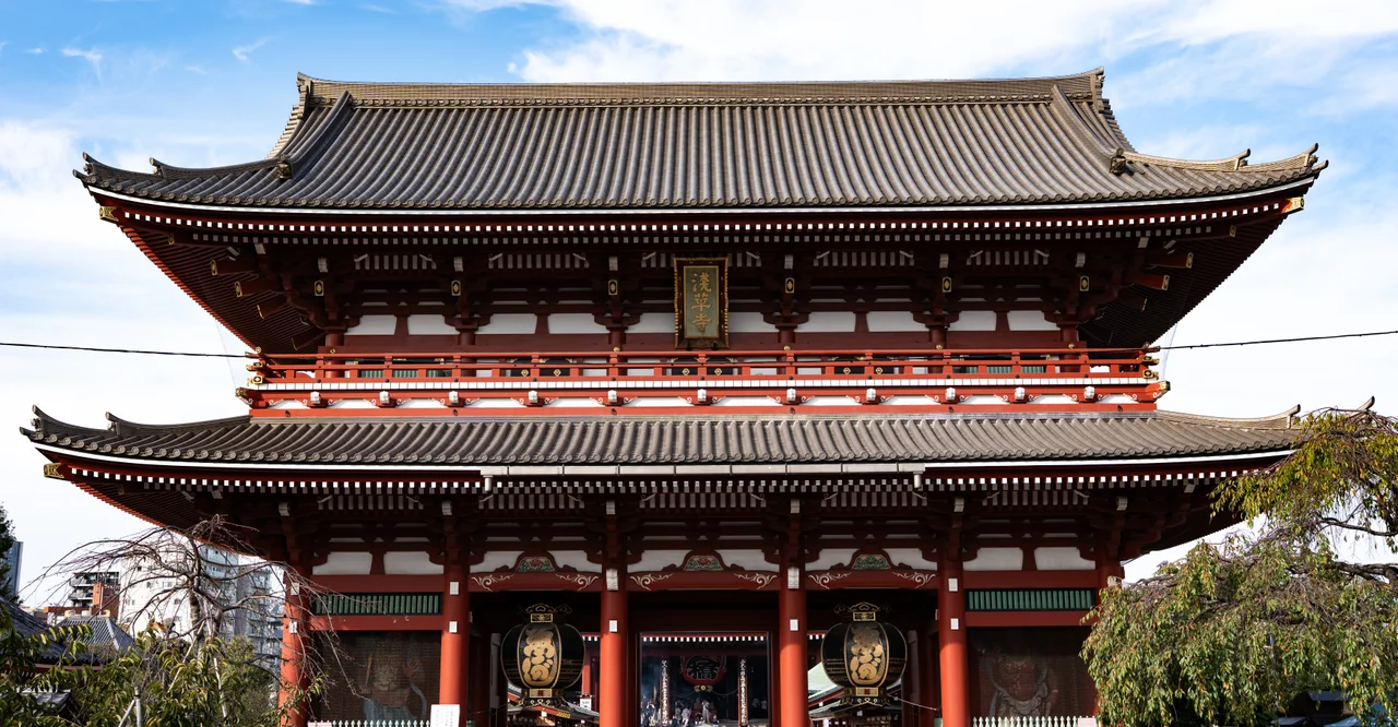 Grande porte de temple à deux toits, rouge et blanche, sous un ciel bleu.