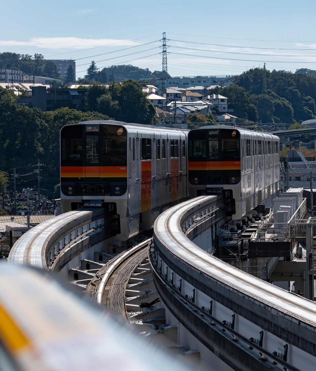 Deux rames de monorail se croisent sur des voies courbes, au-dessus d'une ville bordée de collines.