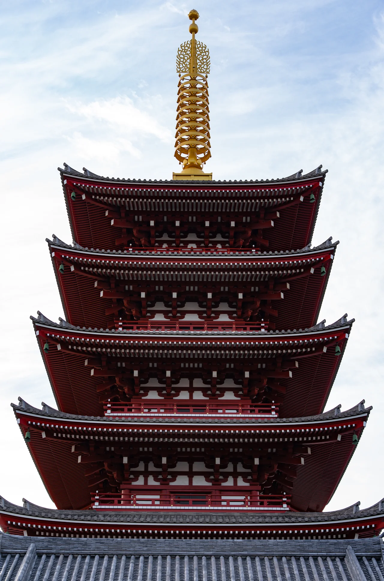 Pagode rouge à cinq étages et sa flèche dorée, vue en contre-plongée sur un ciel blanc.