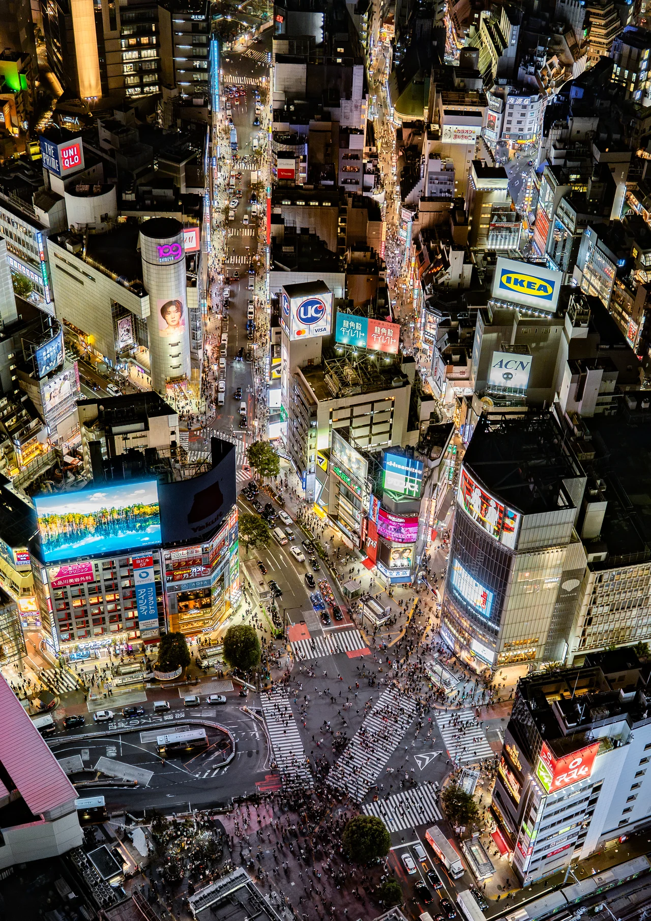 Le carrefour de Shibuya vu d'en haut, de nuit, entouré d'immeubles couverts d'écrans lumineux.